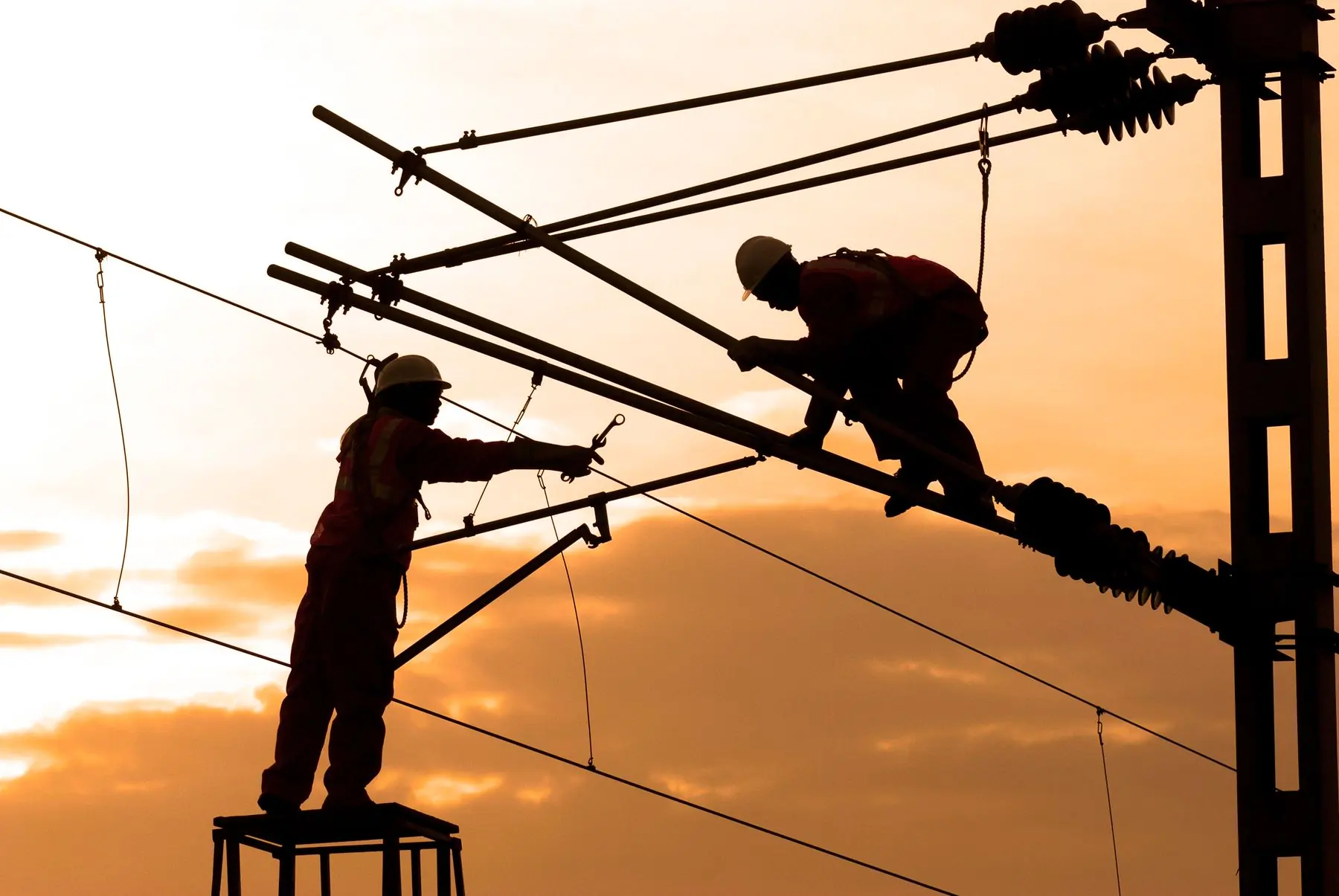 Cuadrilla de linieros trabajando sobre una línea aérea de alta tensión al atardecer